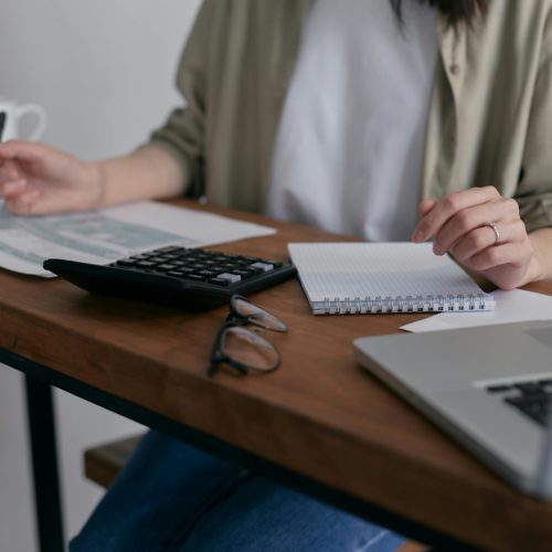 Tisch mit Laptop, Papieren, einem Taschenrechner und Tassen darauf